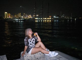 Woman sitting by the waterfront at night with city lights in the background.