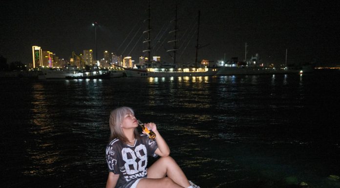 Woman sitting by the waterfront at night with city lights in the background.