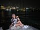 Woman sitting by the waterfront at night with city lights in the background.