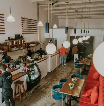 Bright and inviting coffee shop interior with people working, featuring stylish decor and pendant lighting.