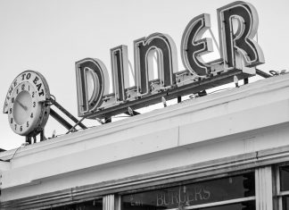 Black and white photo of a vintage diner sign with a clock in Somerville, MA.