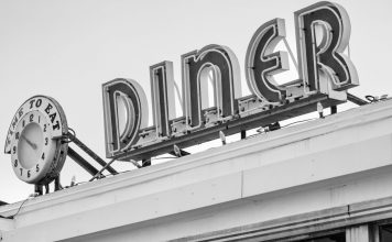 Black and white photo of a vintage diner sign with a clock in Somerville, MA.