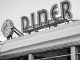 Black and white photo of a vintage diner sign with a clock in Somerville, MA.