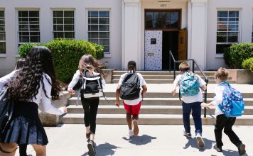 Group of students with backpacks running into school, captured from behind, showing excitement.