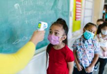 Children wearing masks have their temperature checked in a classroom setting.