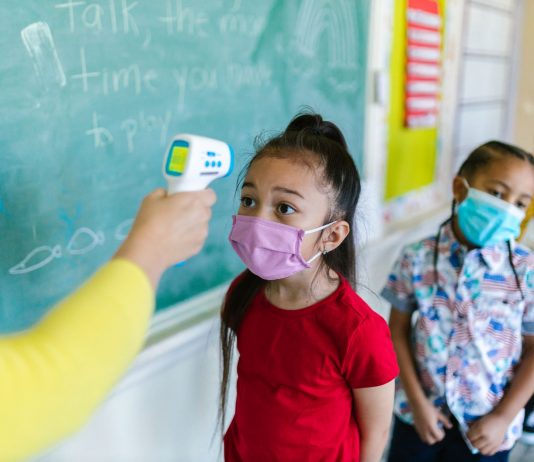 Children wearing masks have their temperature checked in a classroom setting.
