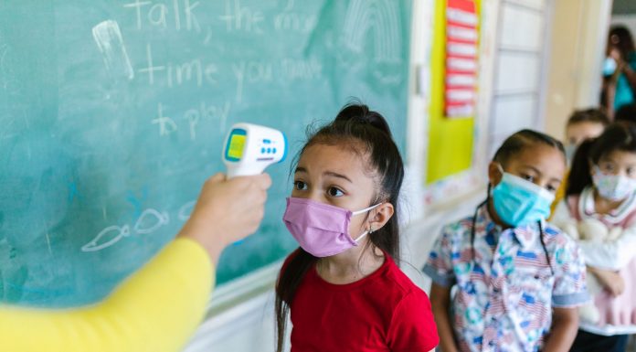 Children wearing masks have their temperature checked in a classroom setting.