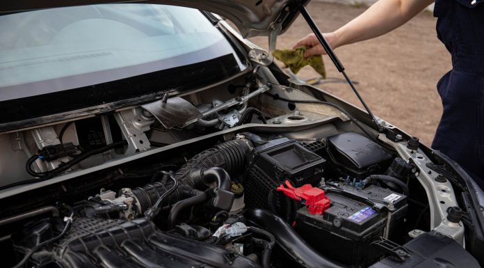 Mechanic inspecting car engine bay and battery during routine maintenance.