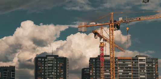 Construction site in Istanbul with cranes and buildings under a dramatic cloudy sky.