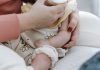 Crop anonymous mother embracing and feeding adorable newborn baby with milk from bottle at home