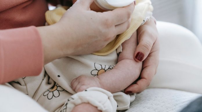 Crop anonymous mother embracing and feeding adorable newborn baby with milk from bottle at home