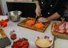 New Jersey City Indian Restaurant Brings Taste of Punjab to Columbus Drive Chef chops carrots on a cutting board surrounded by fresh ingredients in a modern kitchen.