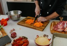 New Jersey City Indian Restaurant Brings Taste of Punjab to Columbus Drive Chef chops carrots on a cutting board surrounded by fresh ingredients in a modern kitchen.