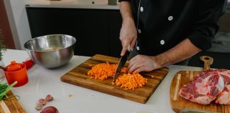 Chef chops carrots on a cutting board surrounded by fresh ingredients in a modern kitchen.