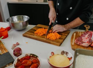 Chef chops carrots on a cutting board surrounded by fresh ingredients in a modern kitchen.