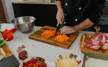 Chef chops carrots on a cutting board surrounded by fresh ingredients in a modern kitchen.
