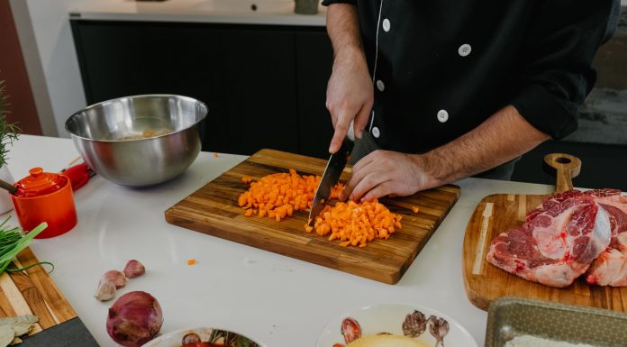 Chef chops carrots on a cutting board surrounded by fresh ingredients in a modern kitchen.