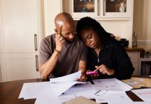 A couple sits at a table managing domestic finances, evaluating documents and using a smartphone.