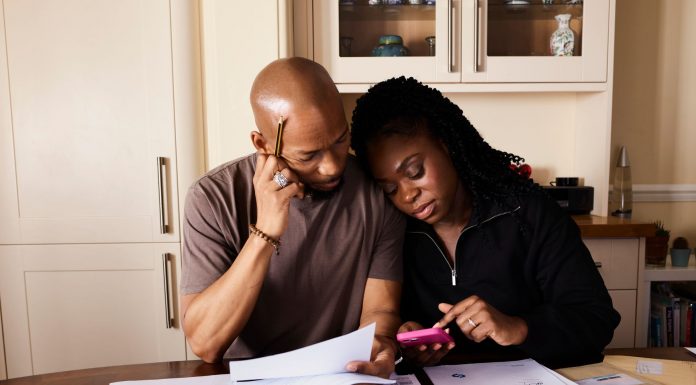 A couple sits at a table managing domestic finances, evaluating documents and using a smartphone.
