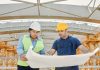 Male and female engineers discussing blueprints at a construction site, promoting teamwork and planning.