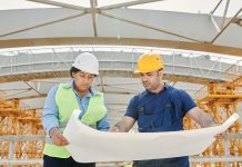 Male and female engineers discussing blueprints at a construction site, promoting teamwork and planning.