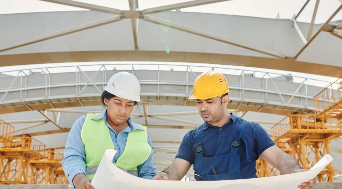 Male and female engineers discussing blueprints at a construction site, promoting teamwork and planning.