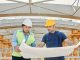 Male and female engineers discussing blueprints at a construction site, promoting teamwork and planning.