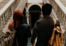Two university students with backpacks walk down a grand staircase in a historic building.