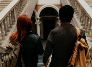 Two university students with backpacks walk down a grand staircase in a historic building.