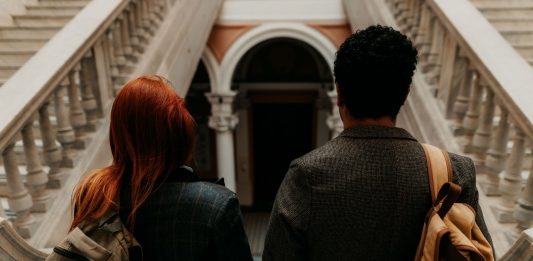 NJCU Officially Becomes Kean Jersey City: What It Means for Students and the Community Two university students with backpacks walk down a grand staircase in a historic building.