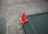 Orange traffic cone placed on a sidewalk edge with wooden planks.