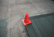 Orange traffic cone placed on a sidewalk edge with wooden planks.