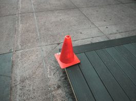 Orange traffic cone placed on a sidewalk edge with wooden planks.