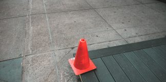 Orange traffic cone placed on a sidewalk edge with wooden planks.
