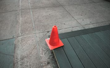 Orange traffic cone placed on a sidewalk edge with wooden planks.