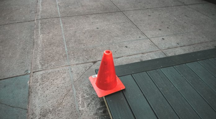 Orange traffic cone placed on a sidewalk edge with wooden planks.