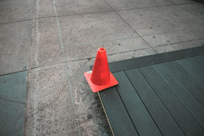 Orange traffic cone placed on a sidewalk edge with wooden planks.