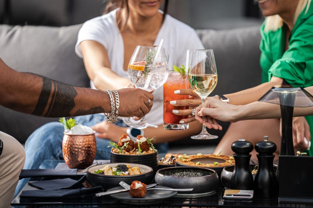 A group of friends enjoying cocktails and snacks at an outdoor gathering, clinking glasses in a cheerful toast.