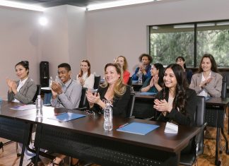 A diverse group of adults applauding in a business seminar setting.