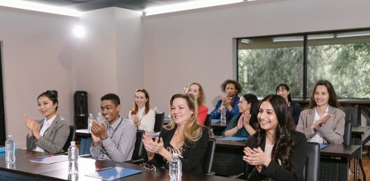 School Board Extends Superintendent’s Contract Five Years Amid Fierce Opposition A diverse group of adults applauding in a business seminar setting.