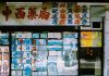 A traditional storefront with Asian script and various posters displayed in the window.