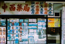 A traditional storefront with Asian script and various posters displayed in the window.