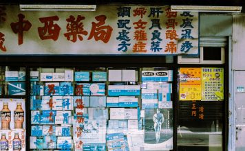 A traditional storefront with Asian script and various posters displayed in the window.