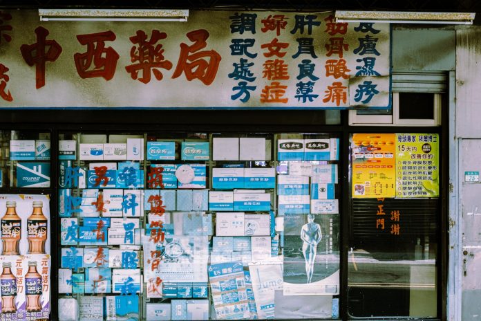 A traditional storefront with Asian script and various posters displayed in the window.