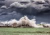 Tornado Warning? What to Expect From Tuesday’s Storms in Jersey City Powerful waves crash against a pier and lighthouse under dark stormy skies.
