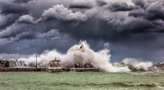 Powerful waves crash against a pier and lighthouse under dark stormy skies.