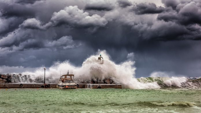 tornado-warning-what-to-expect-from-tuesday-s-stor Powerful waves crash against a pier and lighthouse under dark stormy skies.