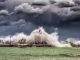 Powerful waves crash against a pier and lighthouse under dark stormy skies.