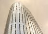Glass skyscraper with window cleaners scaling the facade against a cloudy sky.
