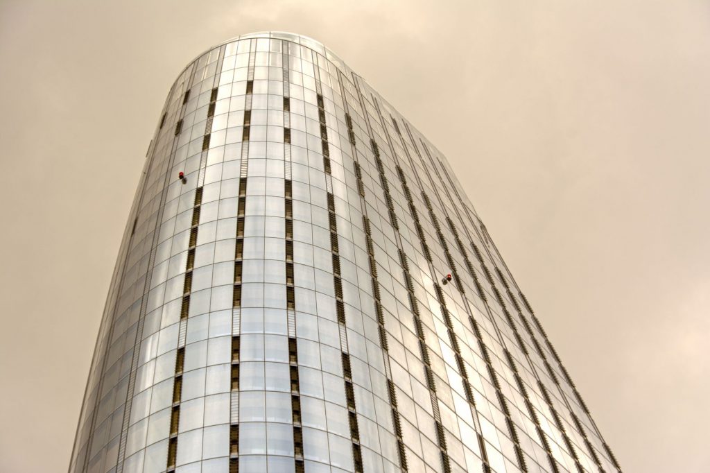 Glass skyscraper with window cleaners scaling the facade against a cloudy sky.